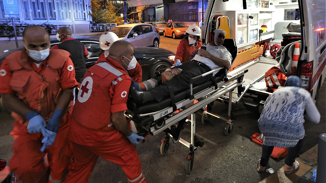 Lebanese Red Cross teams move a wounded man lying on a stretcher into an ambulance.