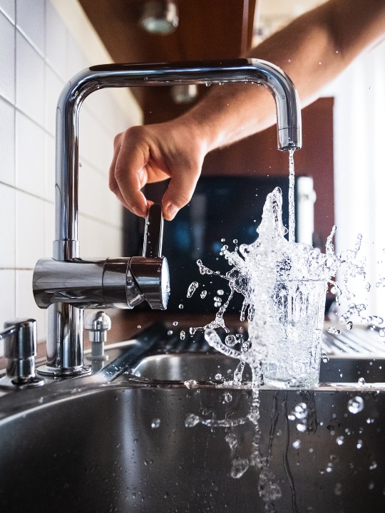 person filling up a glass of water from the tap