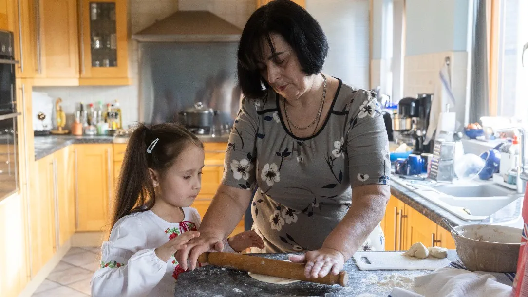 A grandmother and her granddaughter prepare dough together in a kitchen