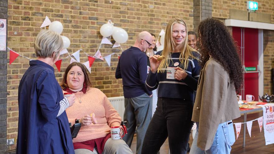 A group stand chatting hold hot drinks with bunting in the background.