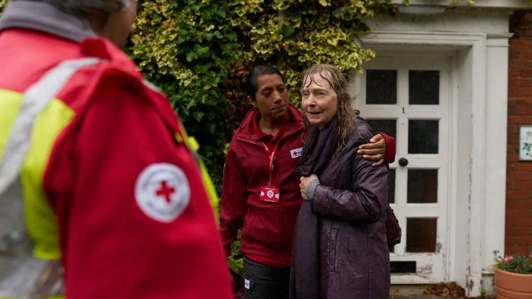 Two British Red Cross volunteers help a shivering woman after a storm and flood.