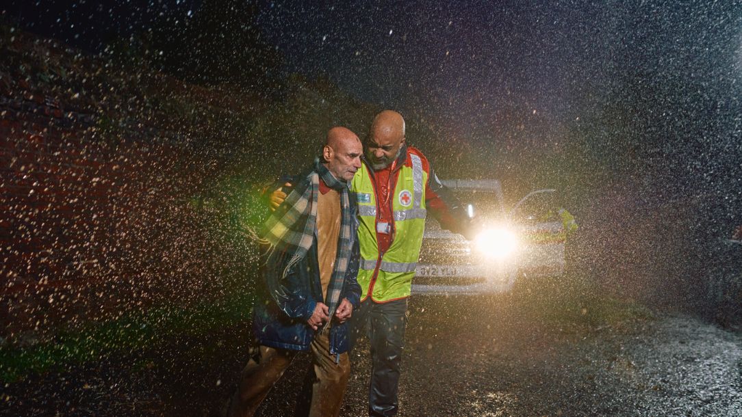 A British Red Cross volunteer leads an older man out of a storm