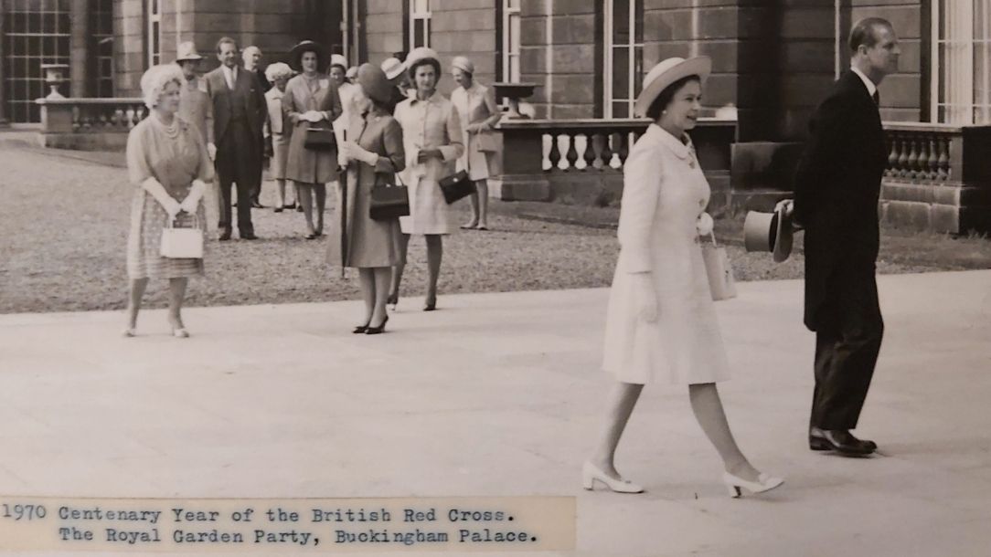 A black and white photograph showing The Queen Elizabeth II walking to a garden party at Buckingham Palace to celebrate the British Red Cross centenary.