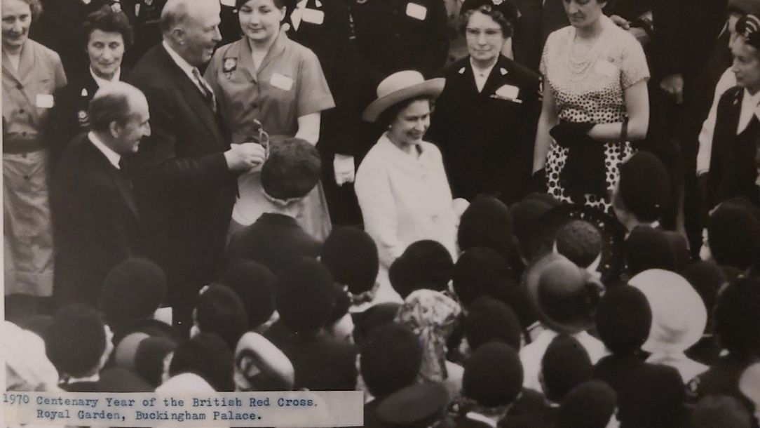 A black and white photograph showing The Queen Elizabeth II walking to a garden party at Buckingham Palace to celebrate the British Red Cross centenary.