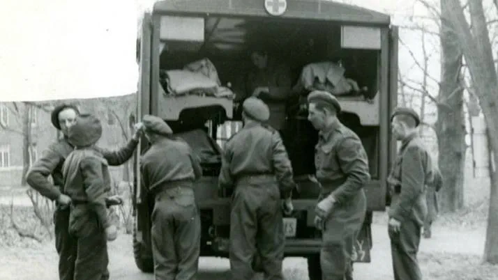 A black and white photograph showing Red Cross volunteers unloading equipment from an ambulance in Normandy.