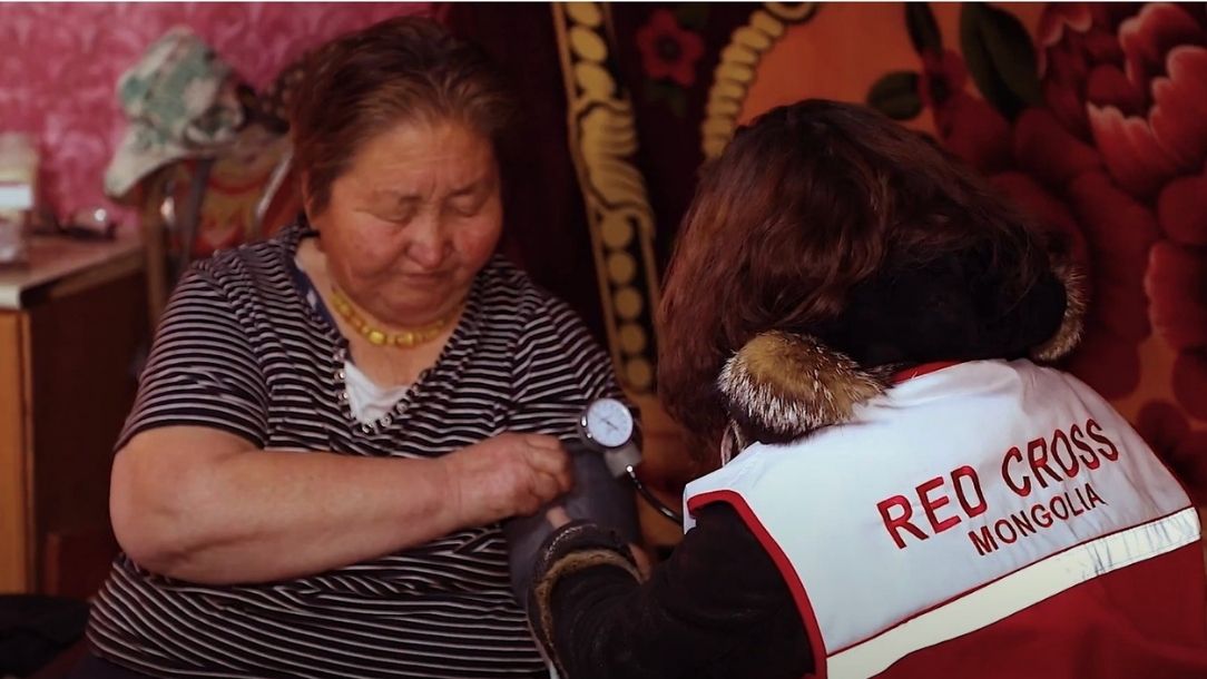 Woman extends her arm while a Red Cross Mongolia volunteer checks her blood pressure.