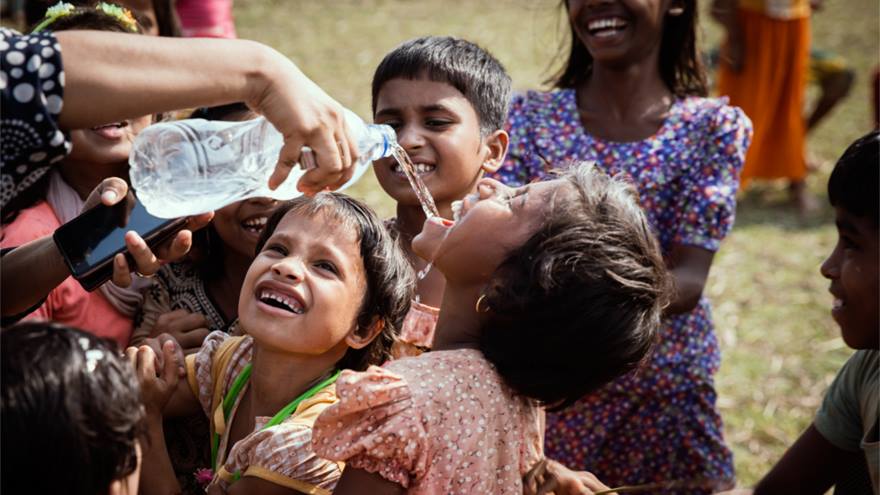 Rohingya children smile as they drink and play with water.	