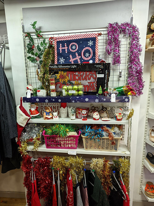 Shelves full of toys and gifts in the British Red Cross charity shop, with tinsel and 'Ho, ho, ho' written on a blackboard.