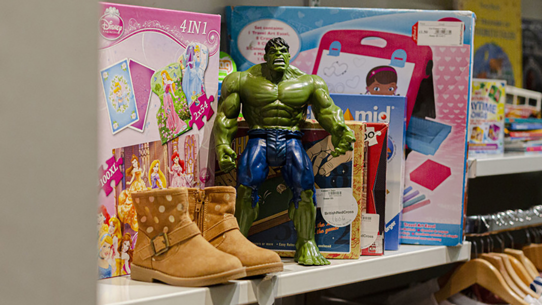 Toys and children's boots sit on a shelf in a British Red Cross charity shop.
