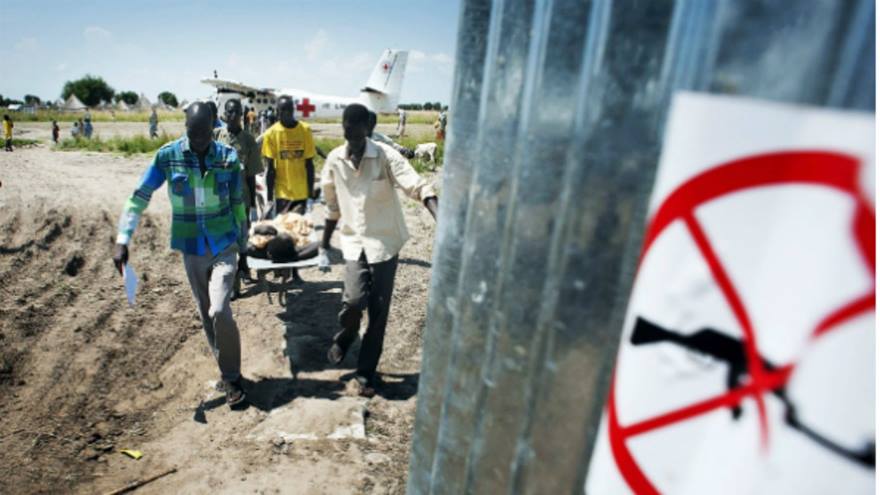 In South Sudan, a medical team runs with a patient on a stretcher with a Red Cross plane in the background