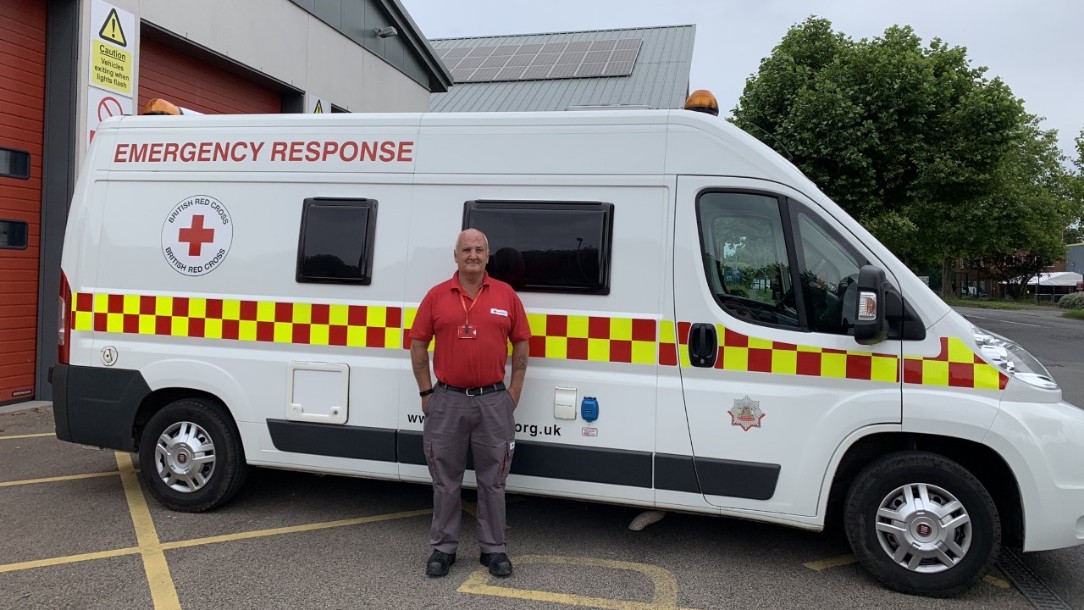British Red Cross volunteer Stephen, in his Red Cross polo shirt, stands in front of a Red Cross ambulance