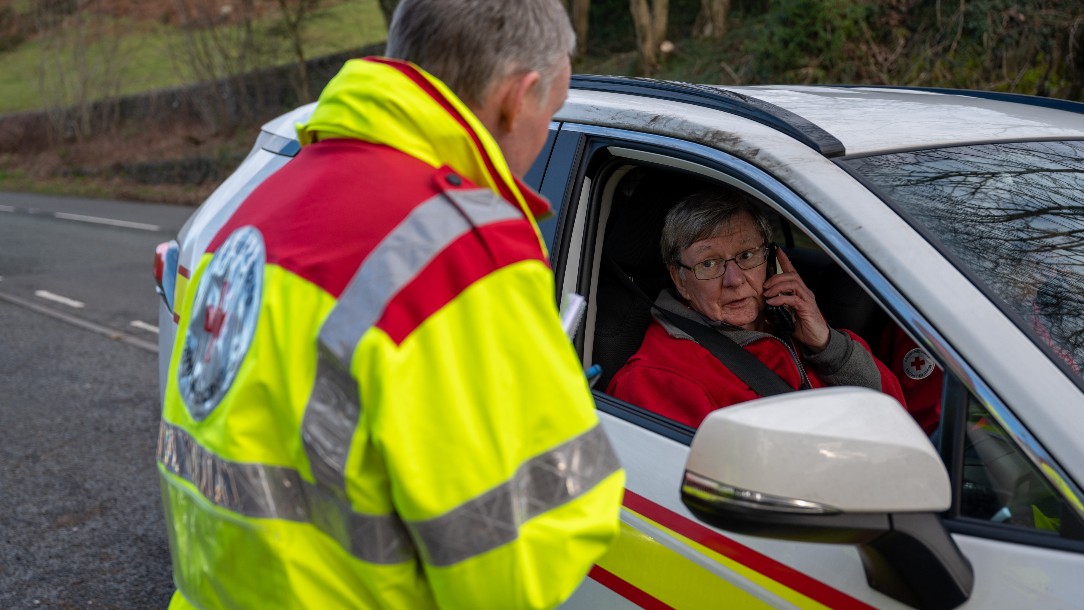 Two emergency response volunteers seen speaking while one sits in the driver's seat of a British Red Cross emergency response vehicle
