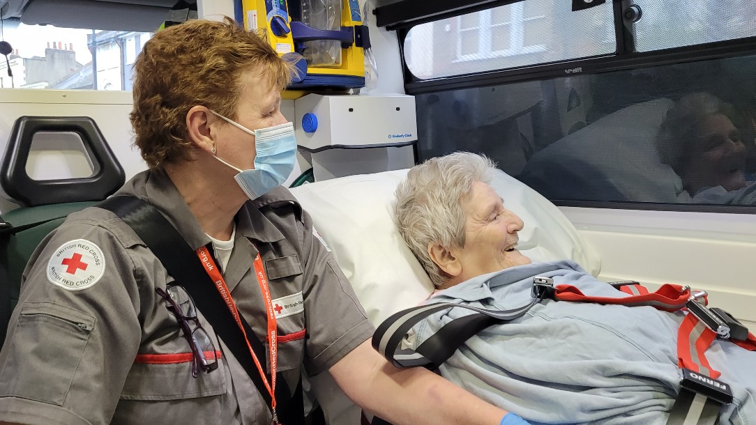 British Red Cross ambulance support staff member sits with service user Sheila in the back of an ambulance