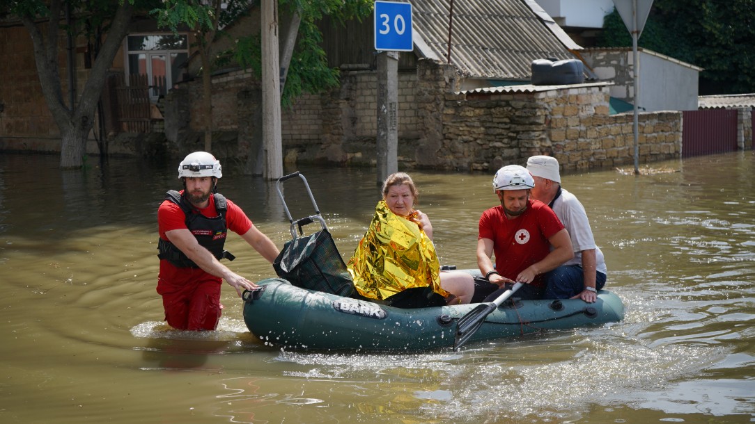 A woman wrapped in a foil sheet is helped out of flood waters in a dinghy by two Red Cross volunteers