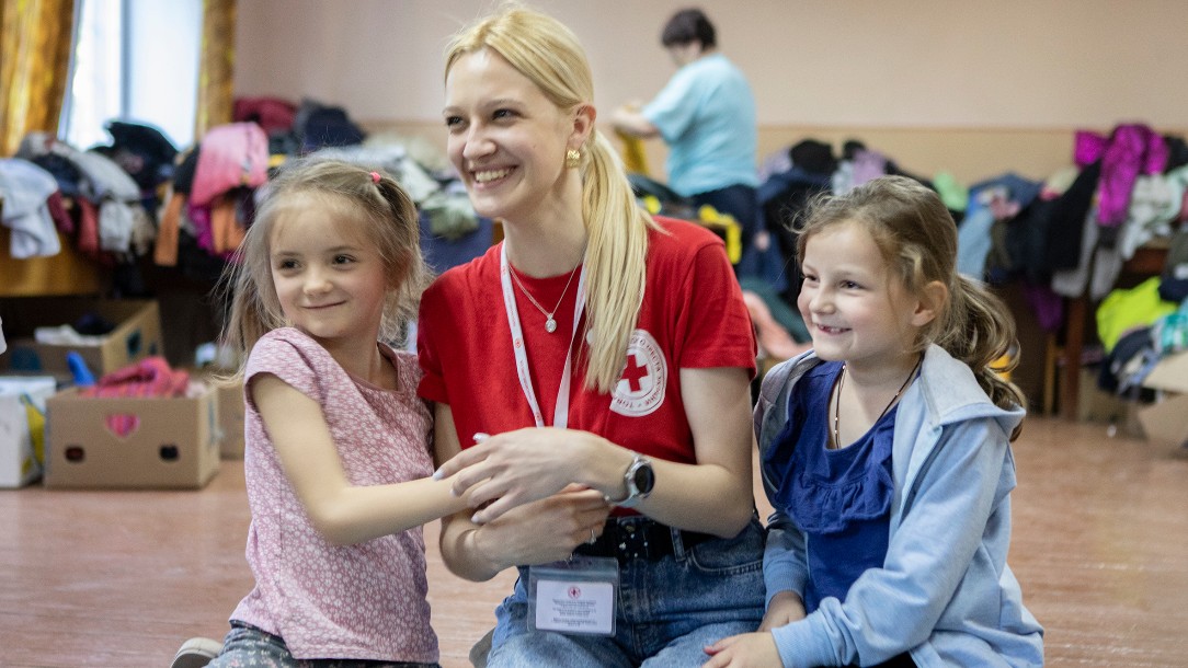 A volunteer from the Red Cross sits between two young girls, all laughing as they attend a psychosocial support session in Uzhhorod, Ukraine