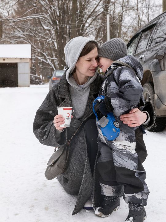 A Ukrainian woman hugs her child in the snow while holding a hot drink provided by the ICRC.