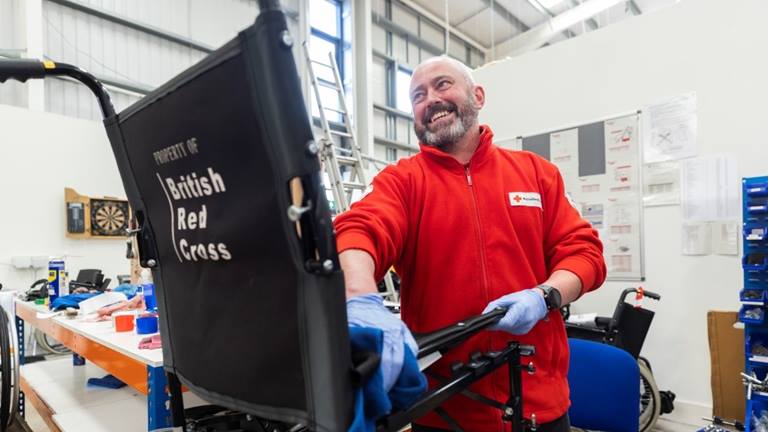 A photograph of a British Red Cross worker cleaning a British  Red Cross wheelchair for hire.