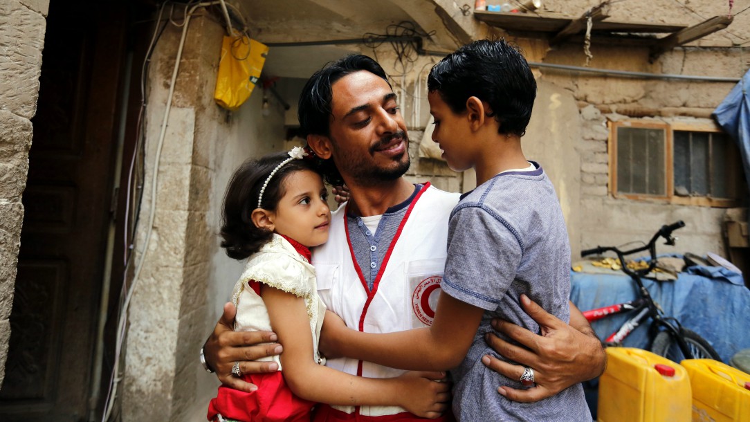 A Yemen Red Crescent volunteer hugs his daughter and son