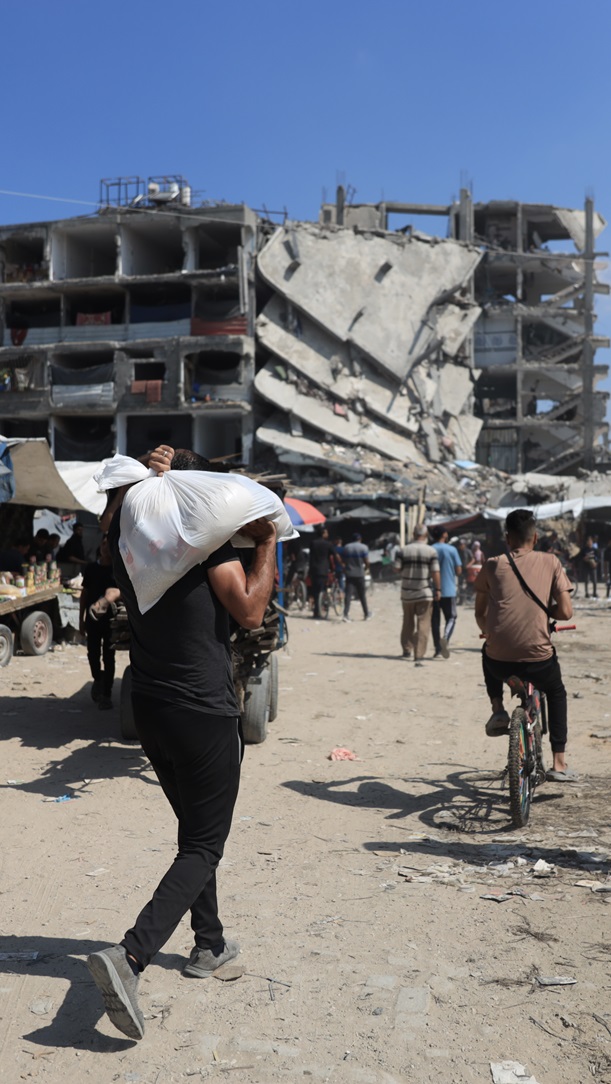 A photo of people walking and cycling, many carrying supplies, through the ruined streets of Gaza.