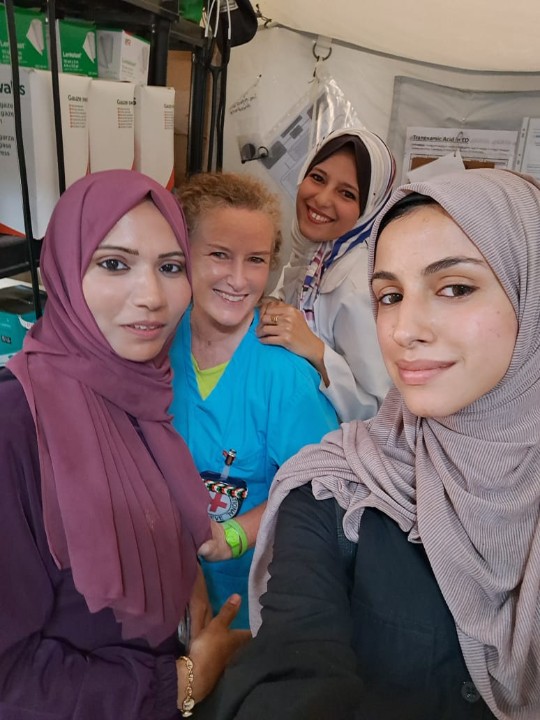 Four women smile at the camera in a selfie taken at the ICRC Field Hospital. One is wearing surgical scrubs.