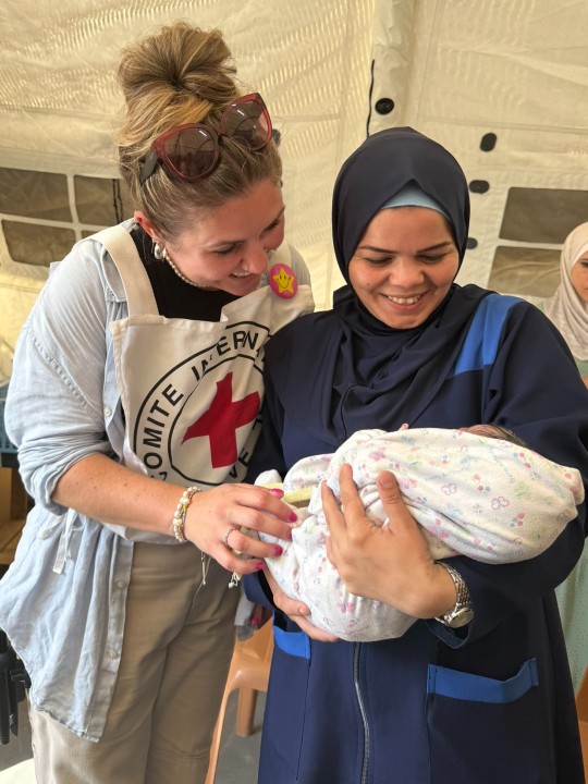 Ghada holds her baby daughter Asia at the Red Cross field hospital in Gaza, while an IFRC worker smiles at the baby
