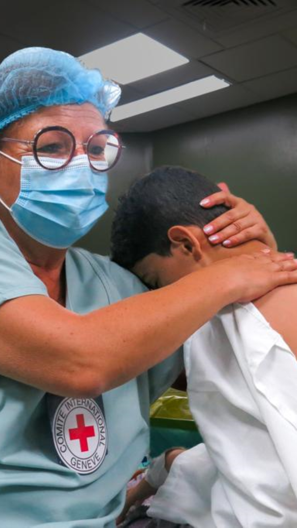 Suzanne, an ICRC Medic, comforts a boy on a hospital bed in Gaza. He leans on her shoulder as she hugs him.