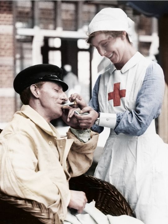 A British Red Cross nurse from the First World War lights a cigarette for a patient in a wheelchair