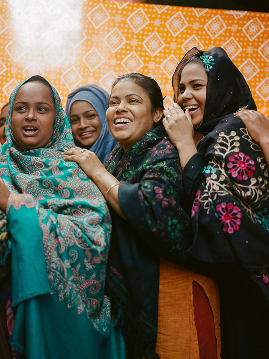 In Banglades, the women of the Hatkhola Womens Squad stand smiling with their arms on each other's shoulders.