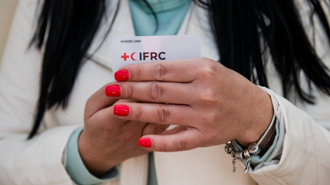 A woman holds up a cash card distributed by the Polish Red Cross. It bears the IFRC logo.