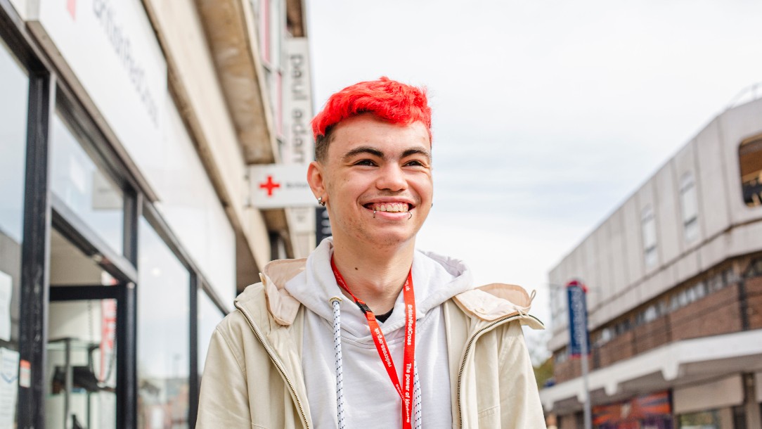 A youth volunteer, CJ, smiles into the distance outside the front of a British Red Cross shop