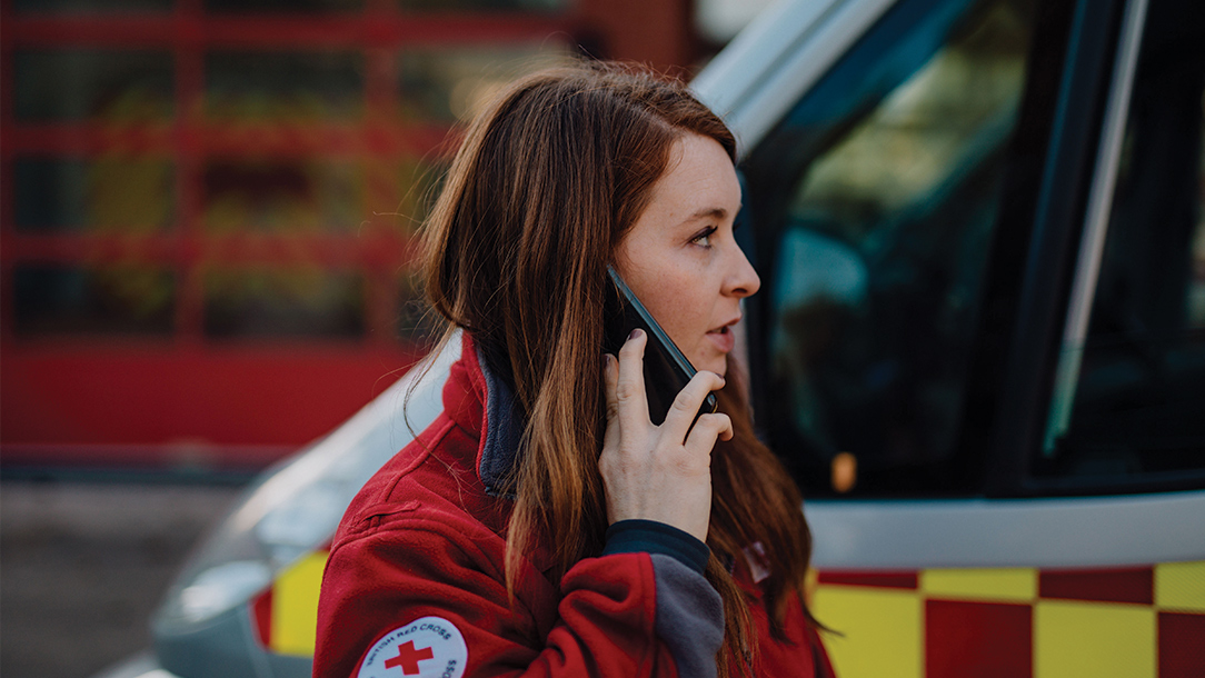 Emergency team member takes a call in front of a British Red Cross ambulance