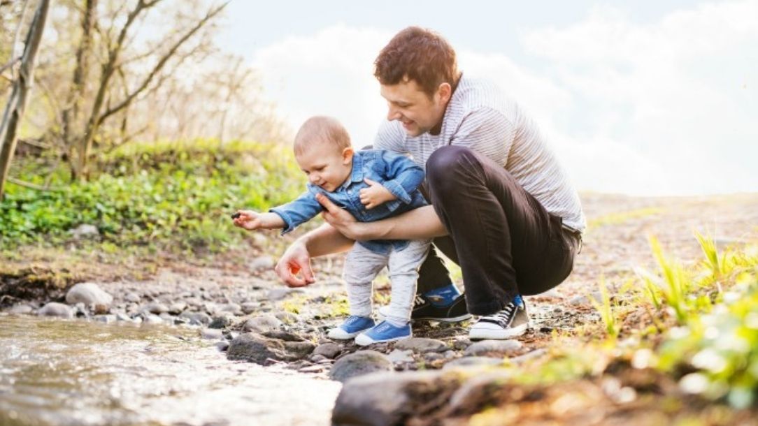 A man and a baby look at something in a stream on a family day out