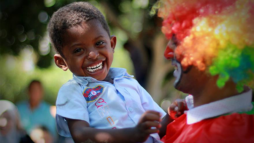 Child smiles as he is held by someone in clown costume