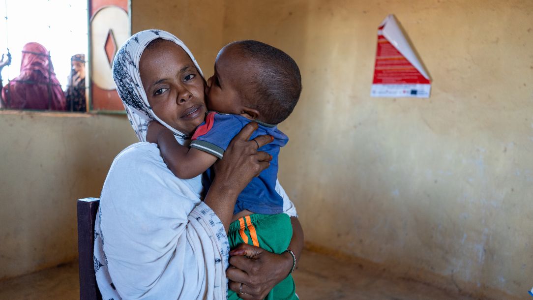 Baby clings on to his mother who holds him