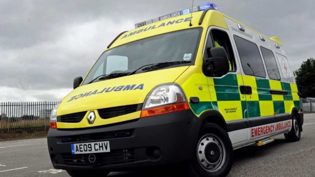 A yellow and green NHS ambulance driving at speed.