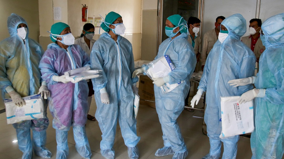 Doctors and medical staff wearing heavy PPE stand together on a hospital ward in India