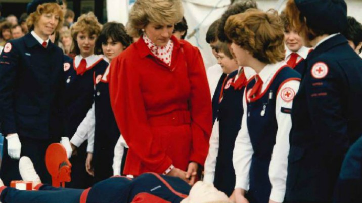 Princess Diana speaks to young people while a CPR mannequin lies on a table.