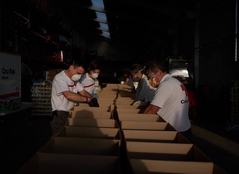 Spanish Red Cross volunteers stand in a row packing food parcels for people affected by coronavirus.