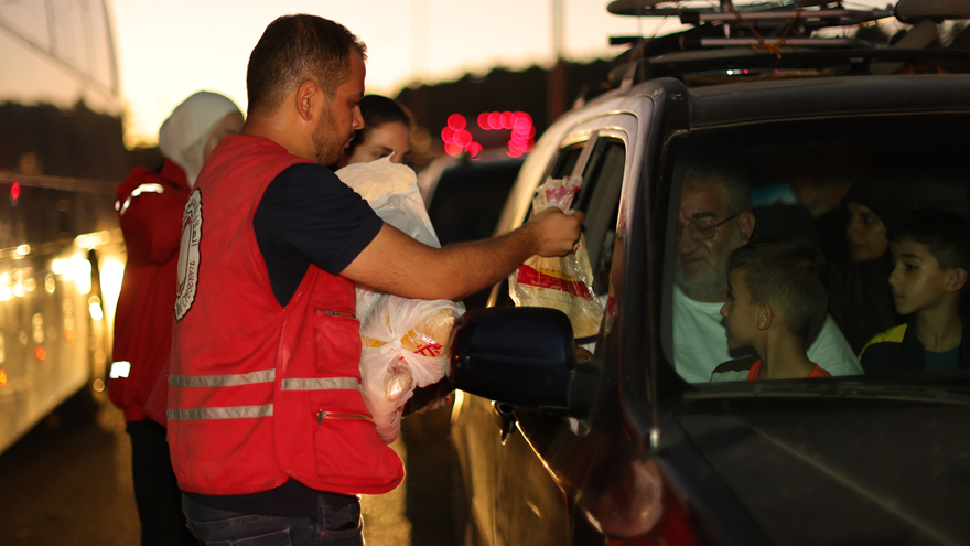 Syrian Arab Red Crescent volunteers give supplies to a family leaving Lebanon is a black car
