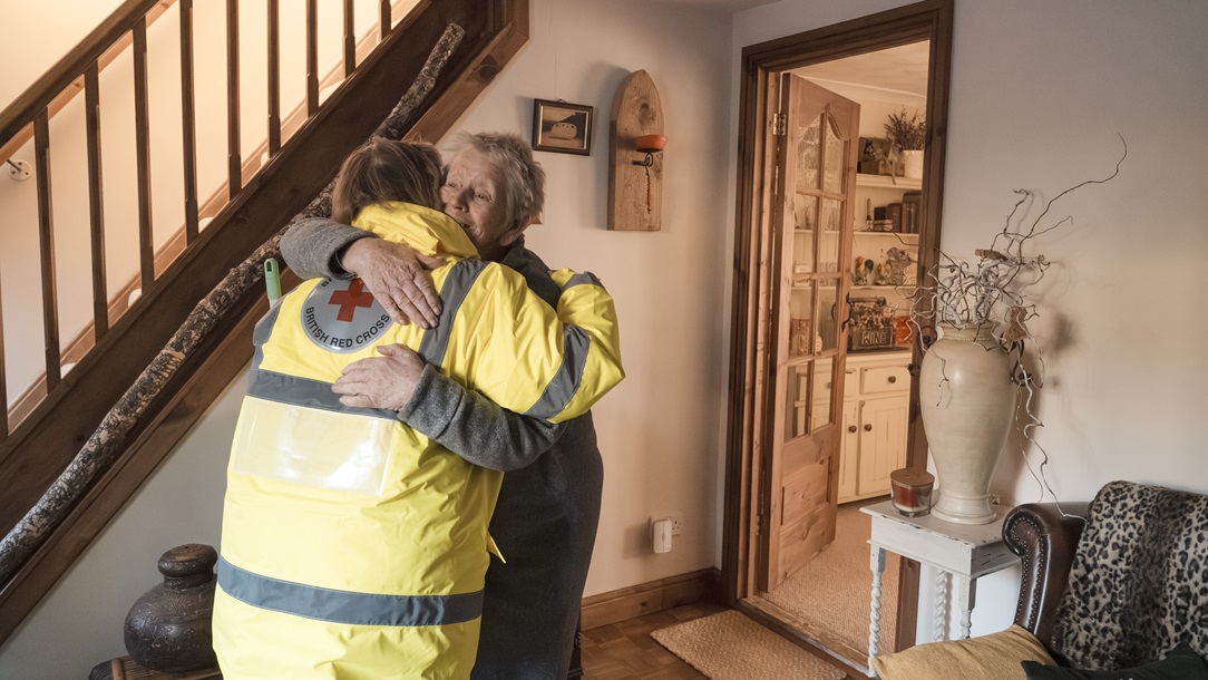 A photo of a Red Cross representative hugging a person to comfort them after their home was damaged by a flood.