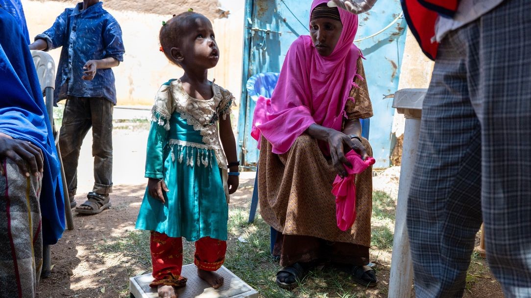 A two-year-old girl called Nimo is being weighed at a mobile health clinic in Qaloàto village, Somalia while her mum looks on anxiously.